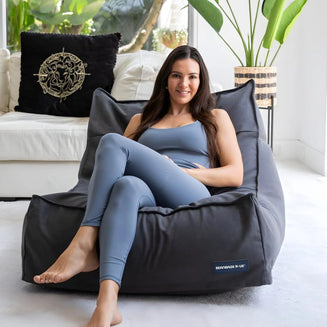 Woman sitting on a gray bean bag chair in a bright room with plants and furniture.