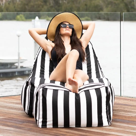 lady with sunglasses & hat, posing on a black and white striped bean bag chair with ottoman on a timber deck