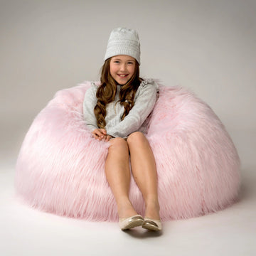 Young girl sitting on a fluffy pink bean bag chair wearing a white hat.